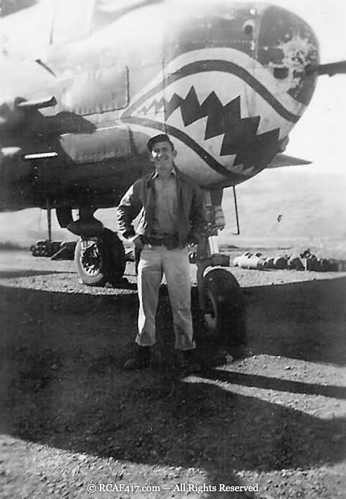 A single airman standing in front of a B-25 with shark-mouth nose art